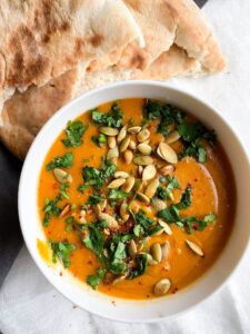 creamy red lentil soup in a bowl topped with toasted pumpkin seeds and chopped herbs