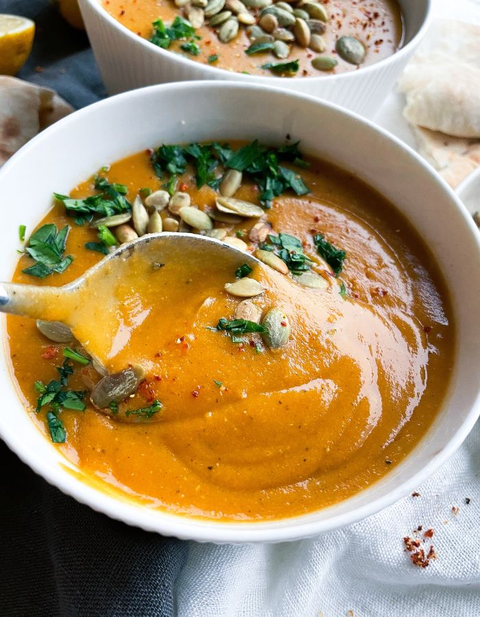 close up of a Creamy lentil soup in a bowl with a spoon inside, topped with fresh chopped herbs and toasted seeds, some red pepper flakes sprinkled on top 