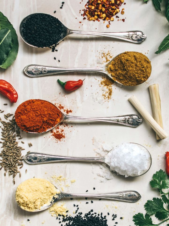 photo from above. flat lay of various Mediterranean spices in spoons and some spices sprinkled on the table and also few herbs laying around