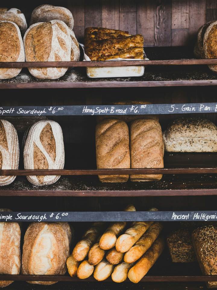 Bakery shleves filled with various types of rustic bread like baguettes, spelt sourdough and others